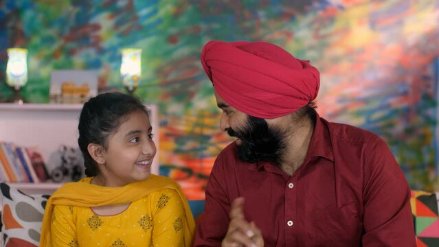 A North Indian Sardar and his little girl doing a Namaste gesture on a video call - greeting  mutual respect  traditional way. An Indian father-daughter chatting online - leisure time  Punjabi fami...