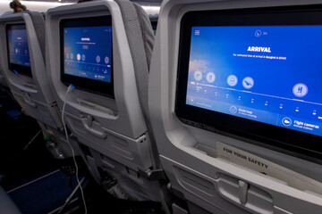 A row of monitors on the back part of seats in a flying airplane