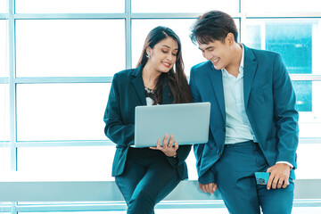 Businessman and businesswoman sitting together with laptop and checking work on window background.