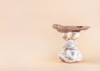 Eco-friendly natural monochrome composition on neutral beige background. Balancing pyramid of  three stones and driftwood, front view, copy space. Harmony and balance. Podium for product presentation.