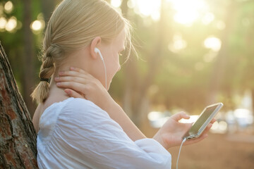 Young teen girl listening to music. Female student girl outside in park listening to music on...