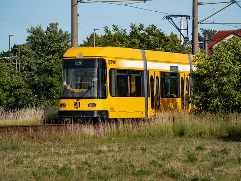 RADEBEUL, GERMANY - 17. June 2022: DVB railcar of the public transportation in the city. Natural area with a yellow tram vehicle on the rails. Sunny summer weather with green bushes and trees.