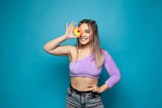 Healthy happy smiling woman looking through colorful donut against blue studio wall background