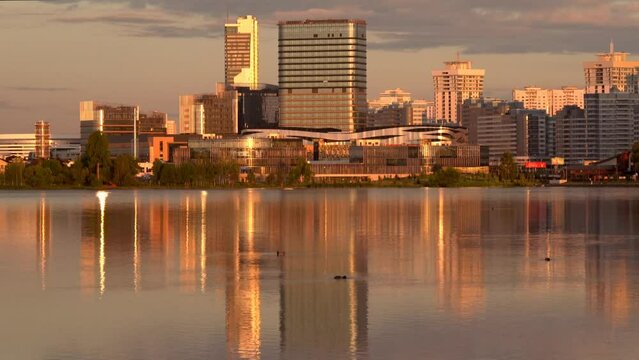 General view of the capital of Belarus - the city of Minsk - from the artificial reservoir Drozdy. At sunset, golden skyscrapers are reflected in the water.