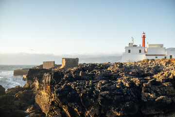 Fototapeta na wymiar Red and white lighthouse in a rocky coast in Portugal