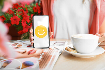 Woman holding phone with happy emoticon on screen in cafe, closeup