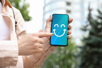Woman holding phone with happy emoticon on screen outdoors, closeup