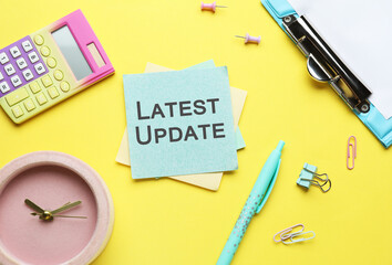 Clock, stationery and paper with text LATEST UPDATE on yellow background