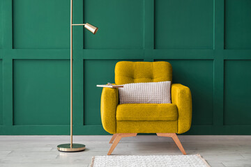 Comfortable armchair and floor lamp near green wall in room