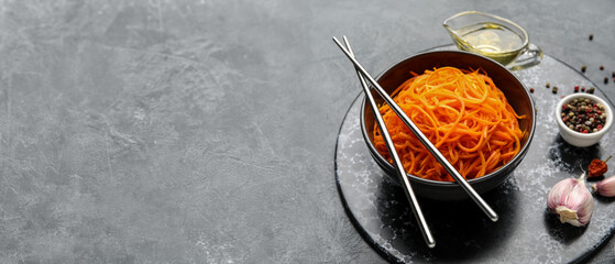 Bowl with spicy Korean carrot salad on dark background with space for text