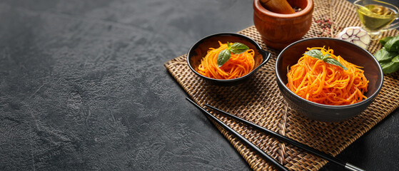 Bowls with spicy Korean carrot salad on dark background with space for text