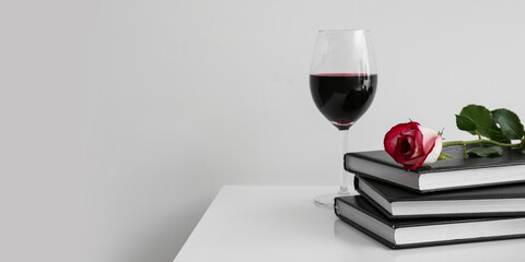 Books, rose flower and glass of wine on table against light background with space for text
