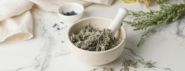 Mortar with dried herbs on white table