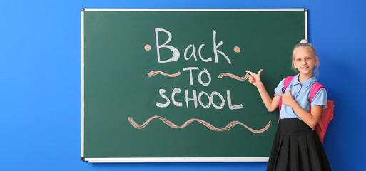 Little girl near blackboard with text BACK TO SCHOOL on blue background