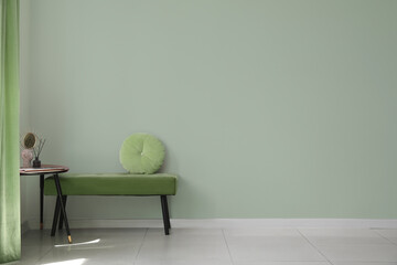 Comfortable bench and pillow with table near light green wall in room