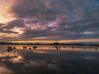 Naklejka premium Aerial sunrise waterscape with boats, reflections and cloud filled sky