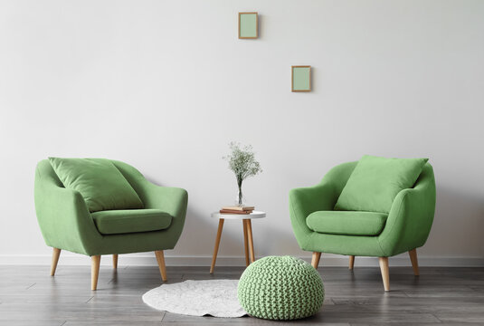 Interior of modern living room with green armchairs, table and pouf near light wall
