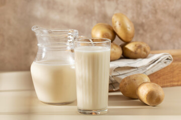 A glass and a jug of potato milk with raw potatoes in a bowl. 