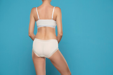 Fototapeta na wymiar Torso of woman wearing white briefs and sport bra, backt view on a blue background