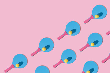 Many blue and pink colourful beach tennis paddle racket with a yellow ping pong ball against pink background. Flat lay pattern with repetition .Outdoors summer activity, fun relax sport idea.