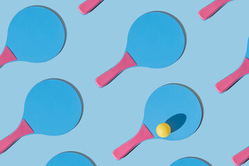 Many blue and pink colourful beach tennis paddle racket with a yellow ping pong ball against blue background. Flat lay pattern with repetition .Outdoors summer activity, fun relax sport idea.