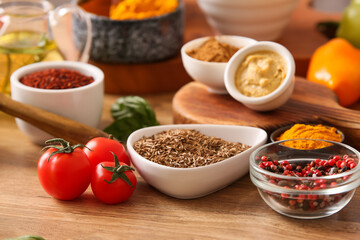 Bowls with aromatic spices and tomatoes on wooden table
