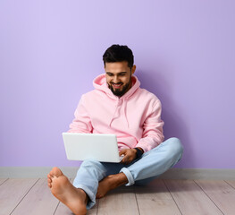 Handsome barefoot man using laptop near lilac wall