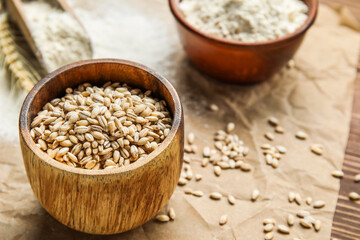 Bowl with wheat grains on parchment paper, closeup