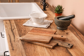 Cutting boards, mortar with pestle and colander on counter near beige wall