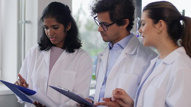 science research, work and people concept - international group of happy scientists with clipboards discussing report in laboratory
