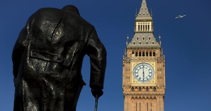 Airplane flying past Big Ben, Houses of Parliament and rear view of the Winston Churchill statue in Parliament Square, Westminster, London, England