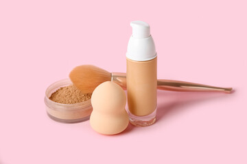 Bottle of makeup foundation, powder, sponge and brush on pink background