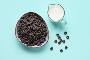 Bowl with black cereal rings and jug of milk on blue background