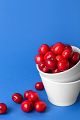Bowls with sweet cherries on blue background