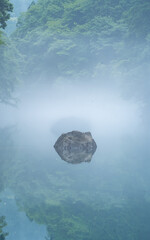 Cold summer season morning in the forest with a lake in Japan, forest reflection and mist weather on the water surface. Green deep water with beautiful small rocks in the lake. Amazing nature  