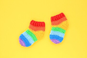 Rainbow handmade crochet gift socks booties on yellow background. Happy motherhood, pregnant,...