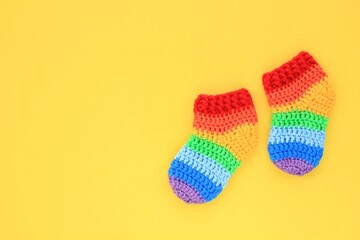 Rainbow handmade crochet gift socks booties on yellow background. Happy motherhood, pregnant, newborn idea. Baby shower greeting card, poster, banner topview concept. Flatlay with copy space. Close up