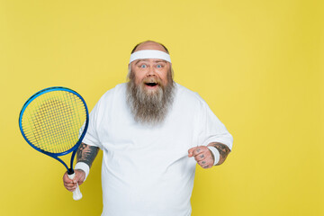 amazed and cheerful overweight tennis player looking at camera isolated on yellow.