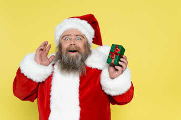 amazed plus size man in christmas costume holding present isolated on yellow.