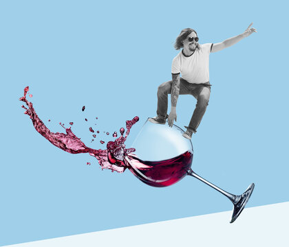 Contemporary art collage. Cheerful young man surfing on red wine glass isolated over blue background. Weekends