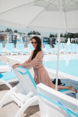 a beautiful girl in a hat is relaxing by the pool and drinking a cocktail, a girl in the pool, summer vacation