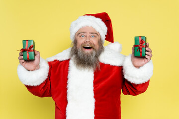 amazed overweight santa claus holding presents isolated on yellow.