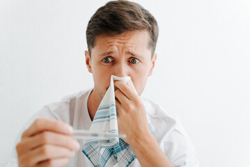 Illness, flu, infection, virus concept. Sick man with symptoms of fever looking shocked at thermometer. Emotional frightened guy holding handkerchief and measuring his temperature - obrazy, fototapety, plakaty