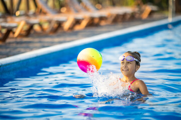A girl in a bright bathing suit swims with an inflatable ball in a pool with clear water on a...