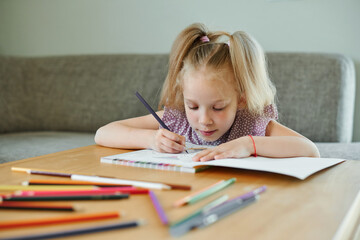 Child girl alone draws and paints of pencils at the table at home. Preschool education and development child concept.