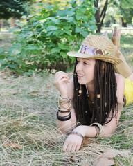 Smiling young woman portrait with dreadlocks hairstyle, dressed in straw hat, posing in a sunny...