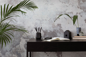 Concrete interior of home office with black desk, image, lamp and office accessories. Grey concrete...
