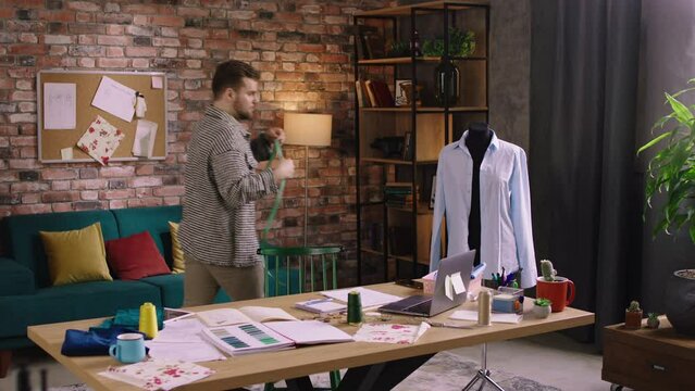 A handsome man with a bushy beard is working on designing clothes as he is measuring up a mannequin. 4k