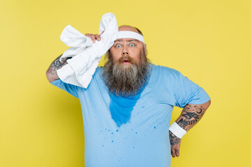sweaty and tired plus size sportsman wiping head with towel isolated on yellow.