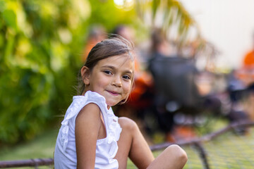 little girl smiling looking at camera over shoulder, with adults blurred in background